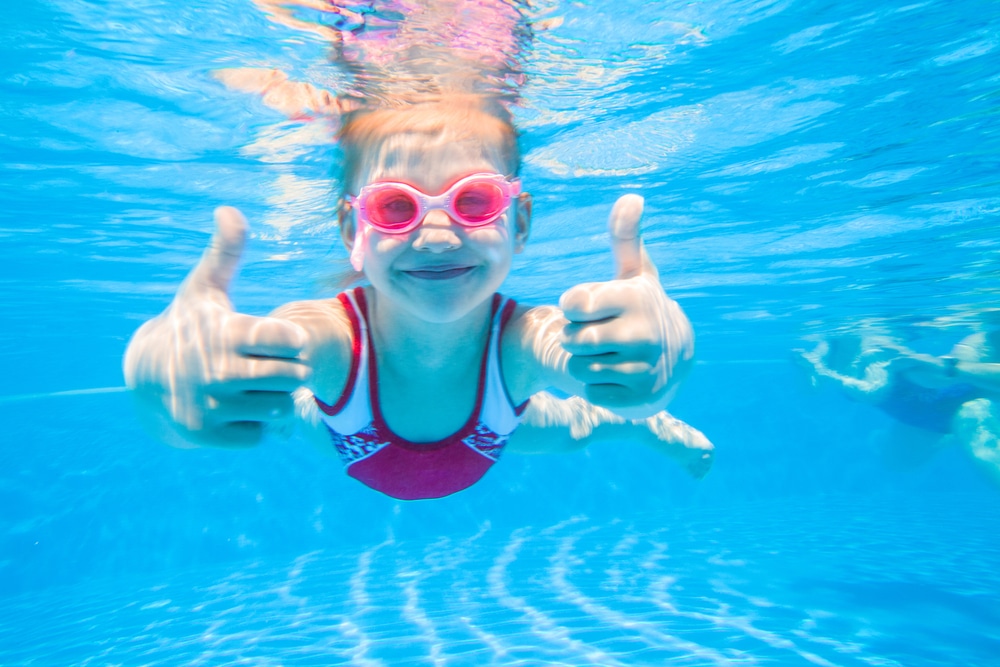 young girl swimming underwater with her thumbs up