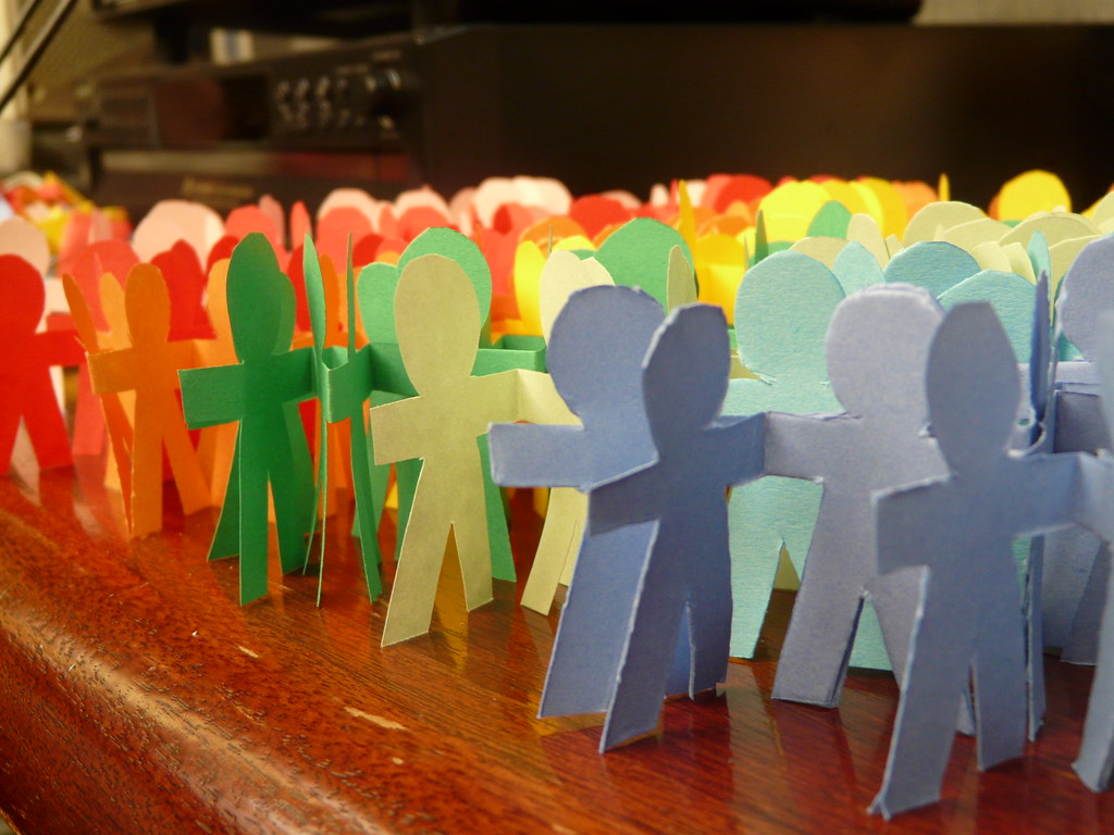 Paper dolls standing in a group - groups of the paper dolls are different colours from orange, green and blue