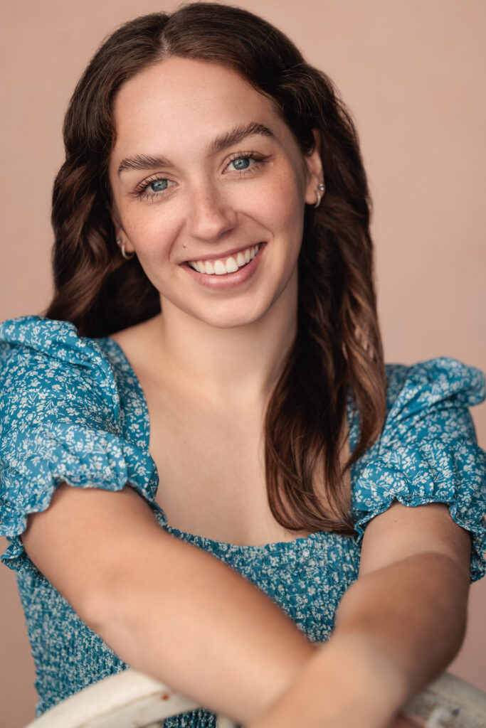 A headshot of Chloe Holder, a while female with medium length brown hair. She is smiling at the camera and is wearing a blue, ditsy floral patterned top.
