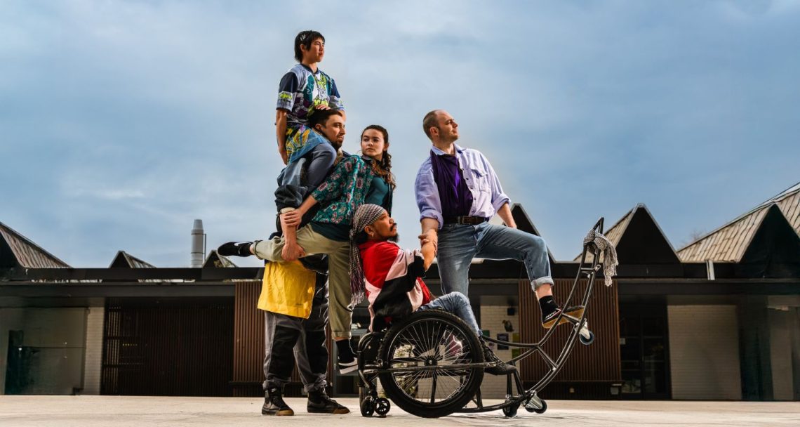 Four dancers pose on and around man in wheelchair